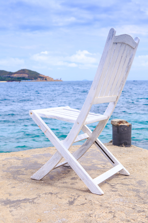 white wooden folding chair on stone pier against transparent azure seaの写真素材