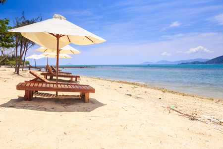 chaise longues under large white umbrellas on golden sand beach against azure sea and blue skyの写真素材