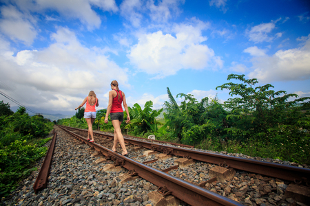 backside view European two young girls in shorts walk along railway past plants against blue skyの写真素材