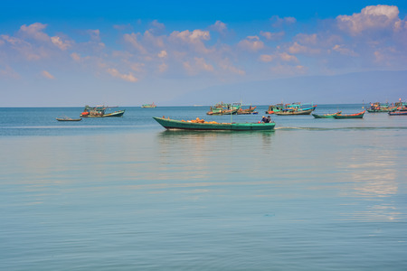 long Vietnamese fishing boats in tranquil azure sea up to horizon against cloudy blue sky at sunriseの写真素材