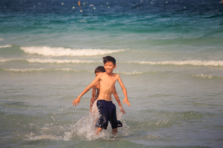 NHA TRANG / VIETNAM - APRIL 16 2017: Happy smiling Vietnamese children play in the ocean waves by beach against azure water on hot sunny day on April 16 in Nha Trangのeditorial素材