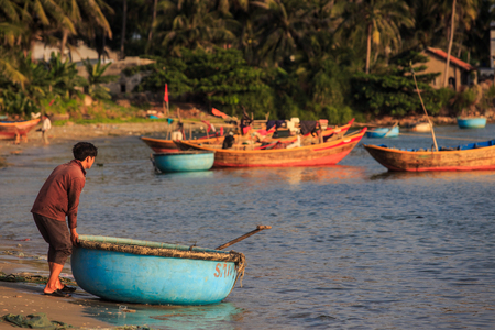 MUI NE / VIETNAM - MARCH 17 2016: Barefoot asian man pushes blue round fishing boat on March 17 in Mui Neのeditorial素材