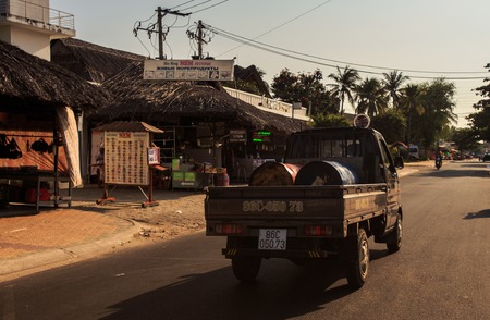 MUI NE / VIETNAM - MARCH 17 2016: Old pickup carrying big metal barrels down empty street