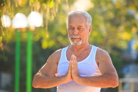 closeup european gray bearded old man shows yoga pose in tropical parkの写真素材