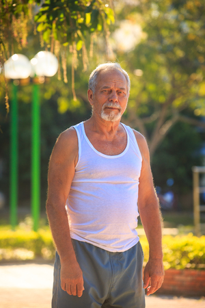 european gray bearded old man in white vest blue shorts ready to doの写真素材