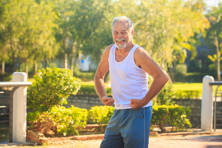 european gray bearded old man does morning exercises strains arms musculars and smile in tropical parkの写真素材