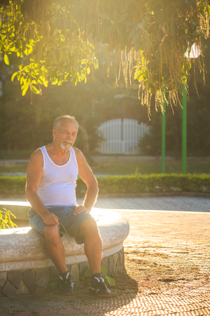 european old man in white vest blue shorts did morning exercises rests on stoneの写真素材