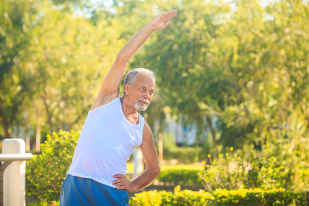 european gray bearded old man does morning exercises right hand up in tropical parkの写真素材