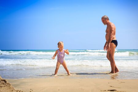 little blond girl and grandfather stand on wet sandの写真素材