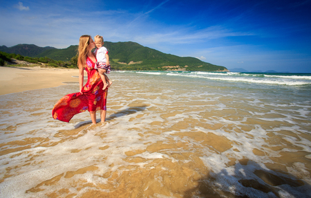 young blond woman in long red dress in foamy wave surf holds claspsの写真素材