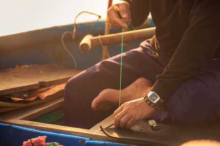 closeup Vietnamese old man hands in watch and bracelet sewing fishing net barefoot on boat benchの写真素材