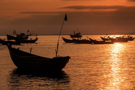 Vietnamese fishing boat silhouette with flagstaff in the sea at bright sunset reflection on surfaceの写真素材