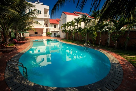 beautiful large oval pool with azure water among green palm trees in hotel yard against deep blue skyのeditorial素材