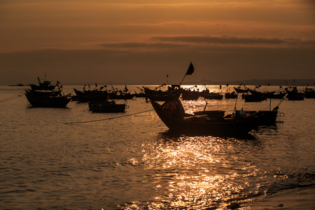 Vietnamese fishing boat silhouettes in sea against bright sunlight reflection of sunset sun pathの写真素材