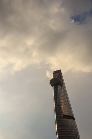 upper storeys of modern fantastic skyscraper against whimsical white and gray clouds in blue skyの写真素材