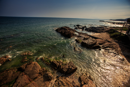 tranquil turquoise sea waves gleam under bright sunlight washing brown rocky beach against blue sky on horizonの写真素材