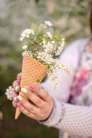 Beautiful waffle cone with ice cream decorated with flowers in the girlâs hand with multi-colored bright manicureの写真素材