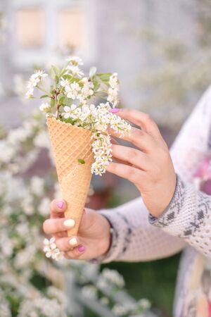 Beautiful waffle cone with ice cream decorated with flowers in the girlâs hand with multi-colored bright manicureの写真素材