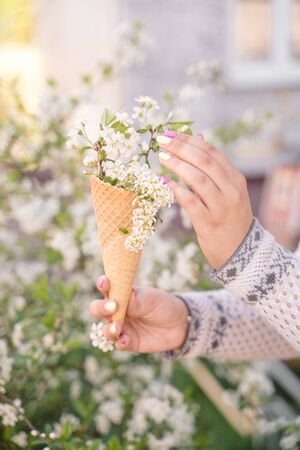 Beautiful waffle cone with ice cream decorated with flowers in the girl's hand with multi-colored bright manicureの写真素材