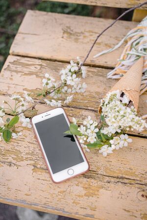 the phone lies on a yellow wooden background with a sprig of a blossoming apple treeの写真素材