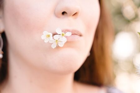 Portrait of a young girl with a blooming apple tree flower in puffy pink lips. Sunny bright day
