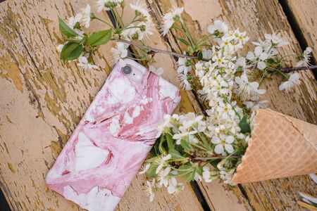 the phone lies on a yellow wooden background with a sprig of a blossoming apple treeの写真素材