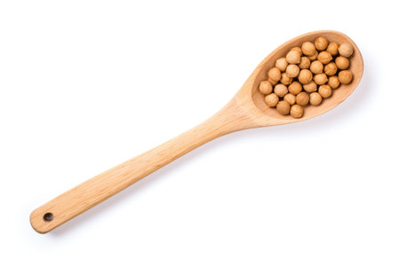 Wooden spoon holding raw organic chickpeas on white background seen from aboveの素材