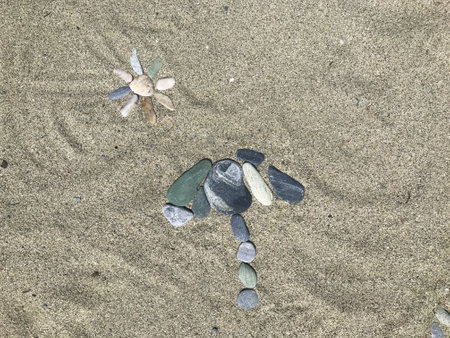 A composite image of small multicolor pebbles arranged on a sand beach show sun and parasolの写真素材
