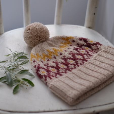 Beige knitted cap of wool with a pompon on a white wooden backgroundの写真素材