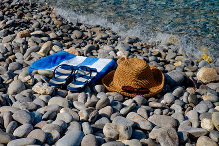 Straw hat, sunglasses, flip flops, towel on a background seascape with a pebble beachの写真素材