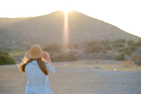 young girl in a hat enjoying the sunset. View from the back