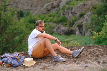 Young stylish man with a beard sitting on a canyon cliff