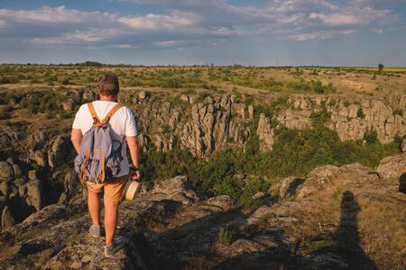 Stylish young man with beard standing on the precipice of the canyon. View from the backの写真素材