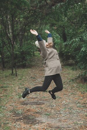 Outdoors lifestyle fashion portrait of pretty young woman walking on the autumn park. Holding maple leaves. Wearing stylish grey coat, sunglasses and glovelettes. Enjoying autumn nature. Autumn colorsの写真素材