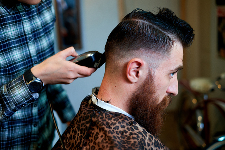 Master cuts hair and beard of men in the barbershop, hairdresser makes hairstyle for a young manの写真素材