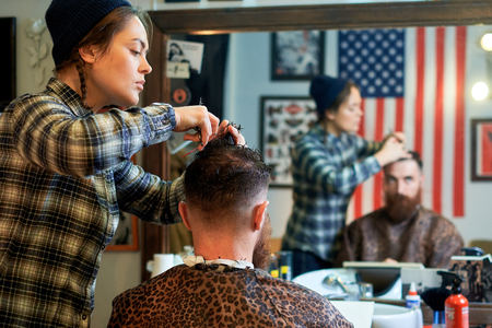 Master cuts hair and beard of men in the barbershop, hairdresser makes hairstyle for a young man