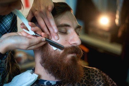Master cuts hair and beard of men in the barbershop, hairdresser makes hairstyle for a young manの写真素材