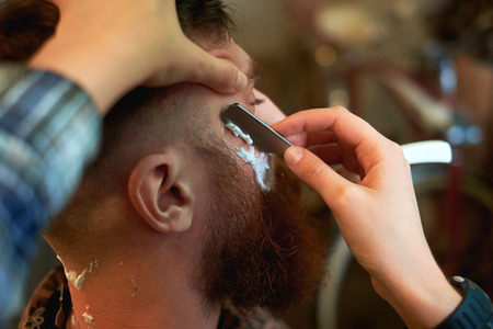 Master cuts hair and beard of men in the barbershop, hairdresser makes hairstyle for a young manの写真素材
