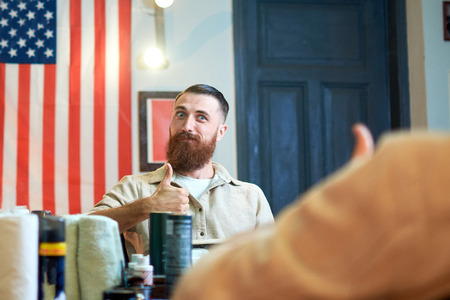 Master cuts hair and beard of men in the barbershop, hairdresser makes hairstyle for a young manの写真素材