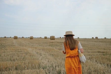 a woman in a straw hat walks along a wheat fieldの写真素材