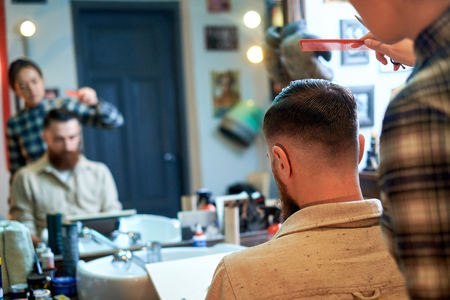 Master cuts hair and beard of men in the barbershop, hairdresser makes hairstyle for a young manの写真素材