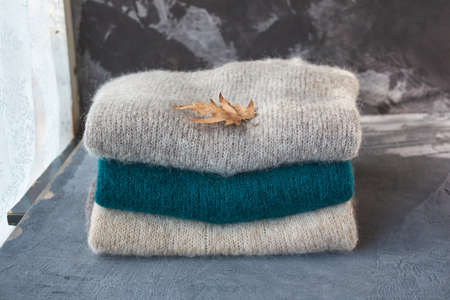 Stack of knitted sweaters with a leaf isolated on the gray background