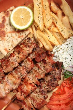 pork skewers served on a plate with fries tzatziki pita and tomato in a greek styleの写真素材
