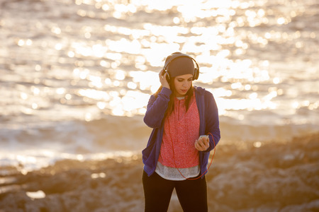 Beautiful young girl with headphones and smartphone at the beachの写真素材