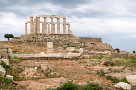 SOUNIO, GREECE - MARCH 27, 2016: Tourists visting and admire the ruins of an ancient Greek temple of Poseidon under dramatic cloudy sky, Cape Sounion, Greeceのeditorial素材