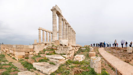 SOUNIO, GREECE - MARCH 27, 2016: Tourists visting and admire the ruins of an ancient Greek temple of Poseidon under dramatic cloudy sky, Cape Sounion, Greeceのeditorial素材