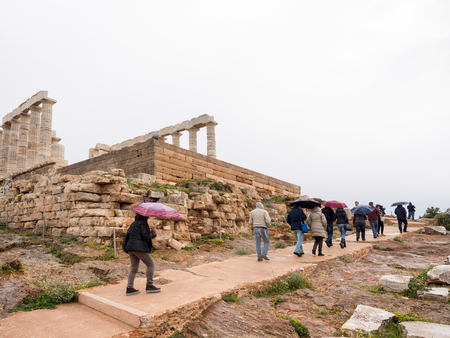 SOUNIO, GREECE - MARCH 27, 2016: Tourists visting and admire the ruins of an ancient Greek temple of Poseidon under dramatic cloudy sky, Cape Sounion, Greeceのeditorial素材