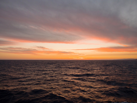 Sunset at the sea with deep orange colors in the afternoon and sky with clouds, view from a shipの写真素材