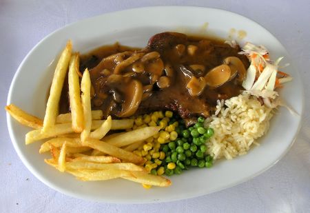 Pork with mushroom sauce, french fries, rice, cabbage, corn and peasの写真素材