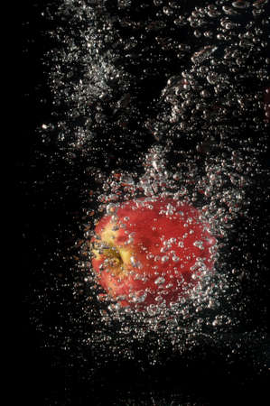 Red apple falling into water on black backgroundの写真素材